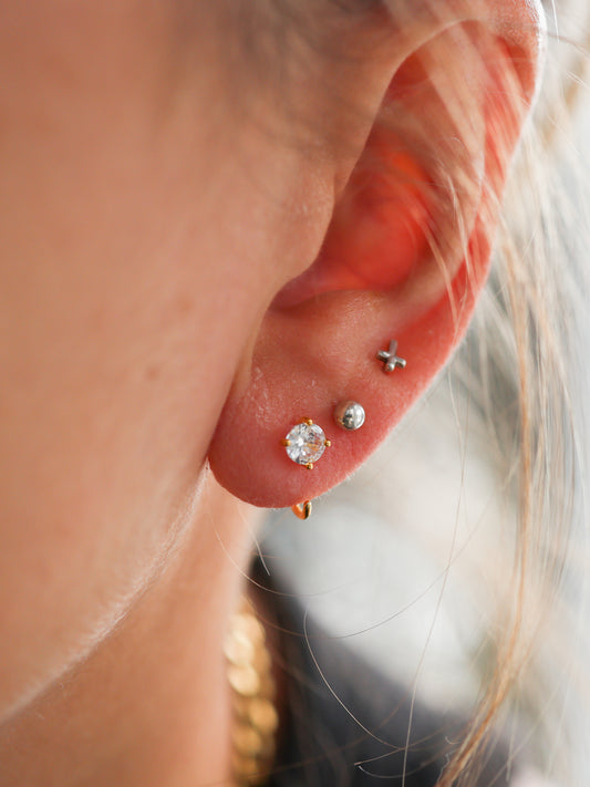 Close-up of ear with minimalist stud earrings, gold and silver, including a crystal stud