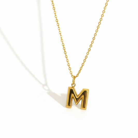 Gold necklace with a minimalist letter M pendant on a simple chain, photographed on white background.
