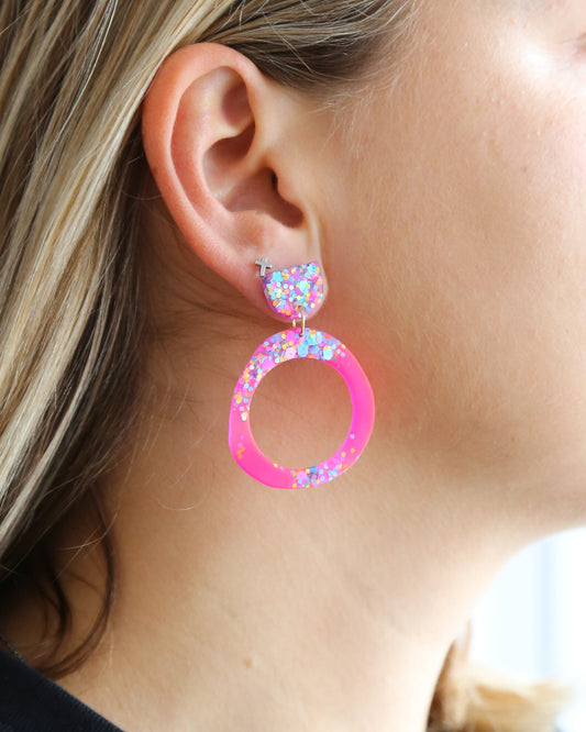 Close-up of a person wearing pink hoop earrings with colorful accents.