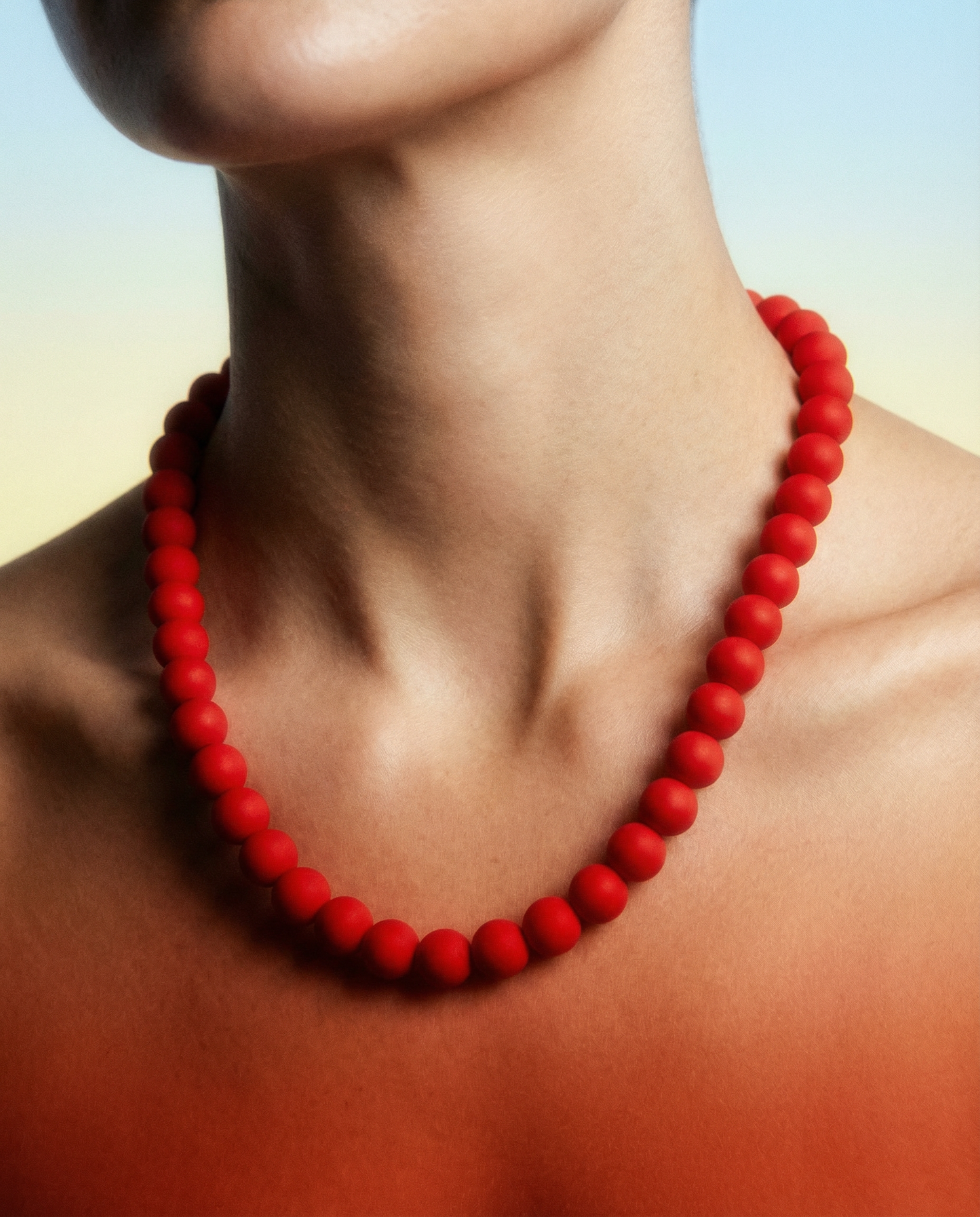Close-up of a woman wearing a bold red beaded necklace against a soft gradient background.