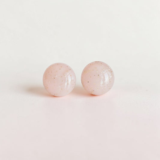 Round minimalist stud earrings with pale pink color and subtle glitter accents