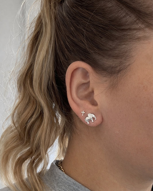 Woman wearing minimalist handmade silver stud earrings, cross and ram design, close-up