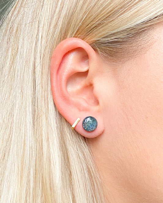 Close-up of an ear wearing a blue gemstone stud earring with a gold post.
