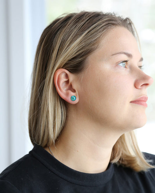 Close-up of a person wearing turquoise earrings with a blurred background