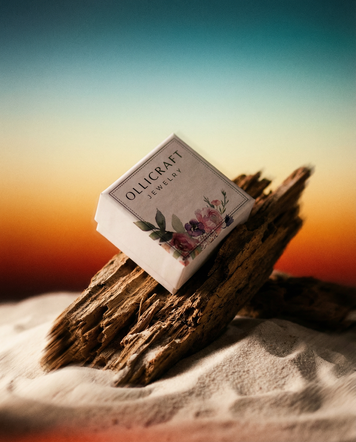 Jewelry box with floral design on driftwood in sand, sunset background, Ollicraft label visible