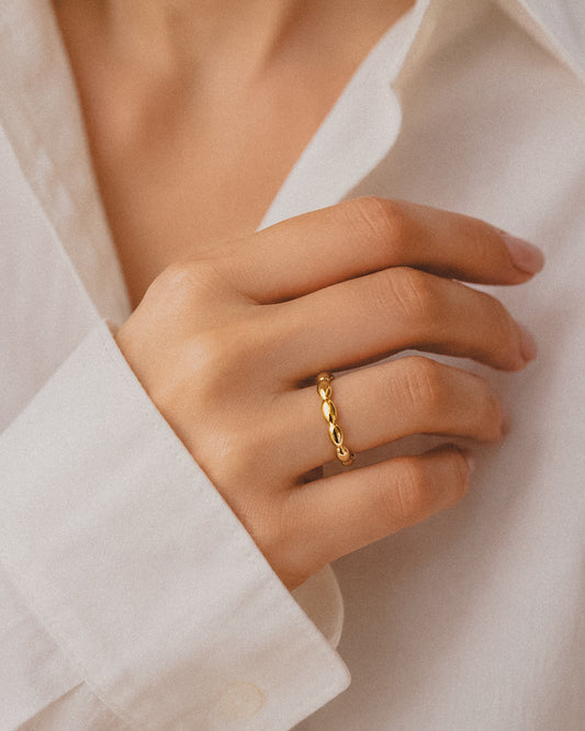 Ollijewelry minimalist gold-tone ring with a delicate beaded design worn on a finger against a white shirt sleeve.