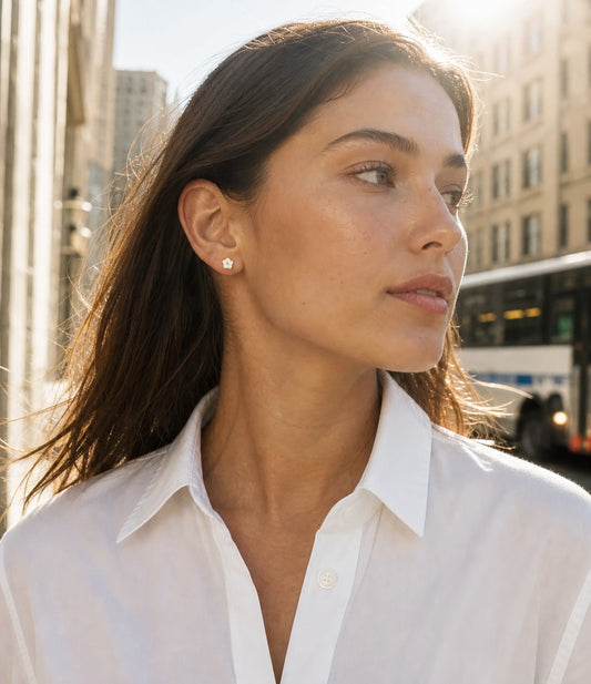 Ollijewelry white flower flat back surgical steel stud earring worn by a woman in a city setting