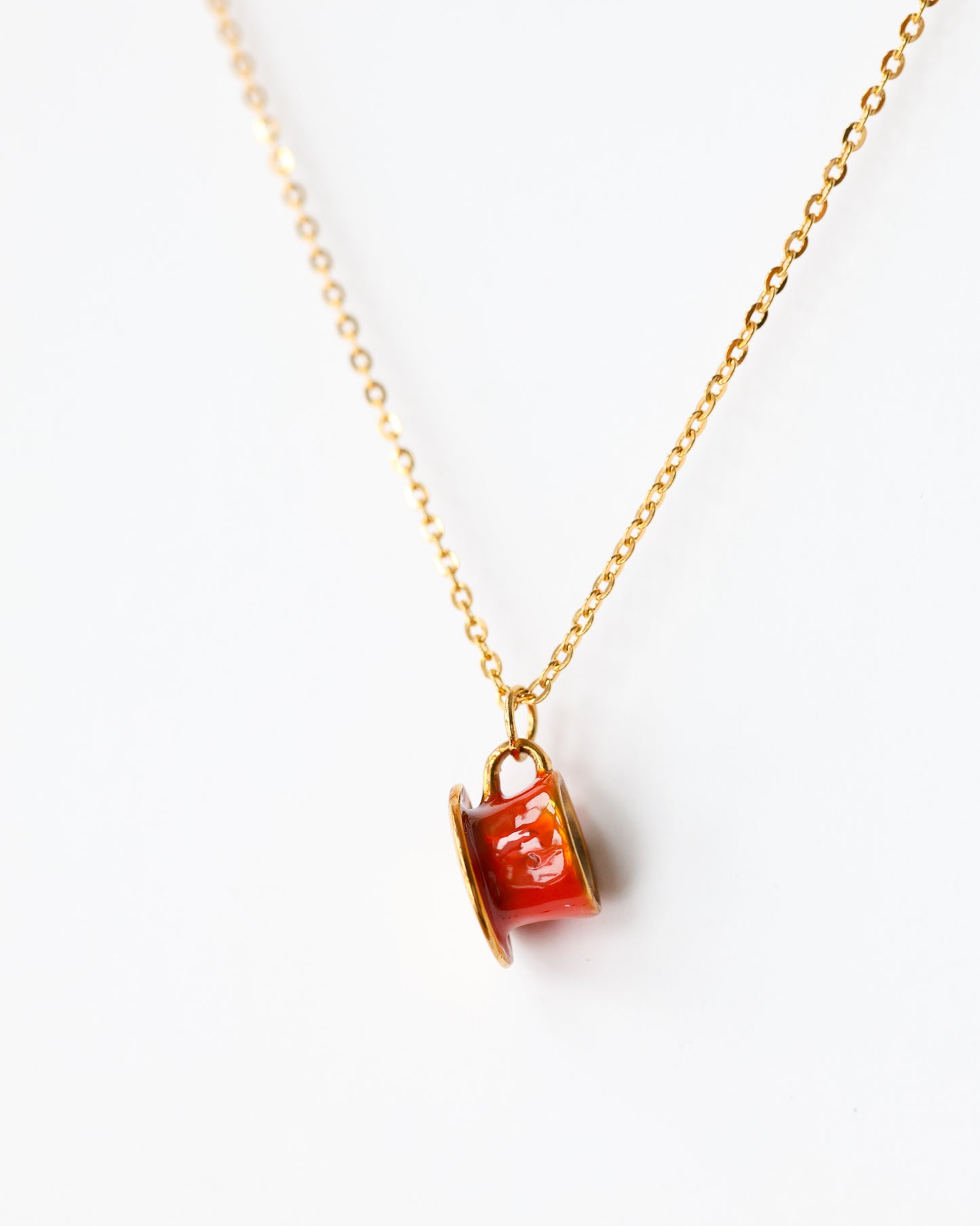 Gold chain necklace with small red enamel charm on white background