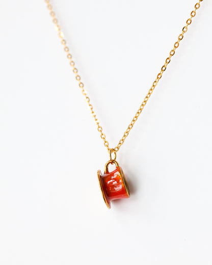 Gold chain necklace with small red enamel charm on white background