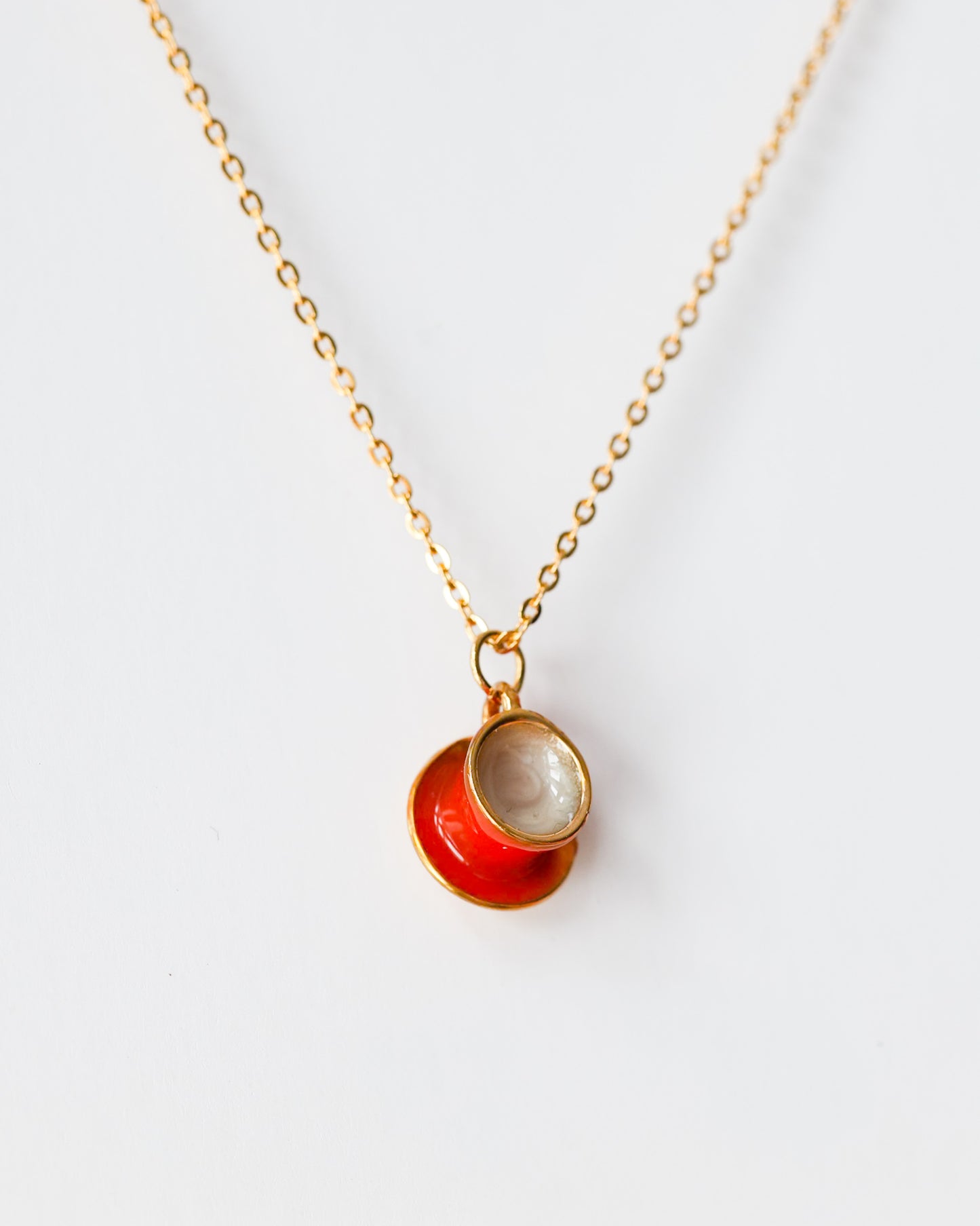 Gold chain necklace with a red enamel teacup and saucer pendant on white background
