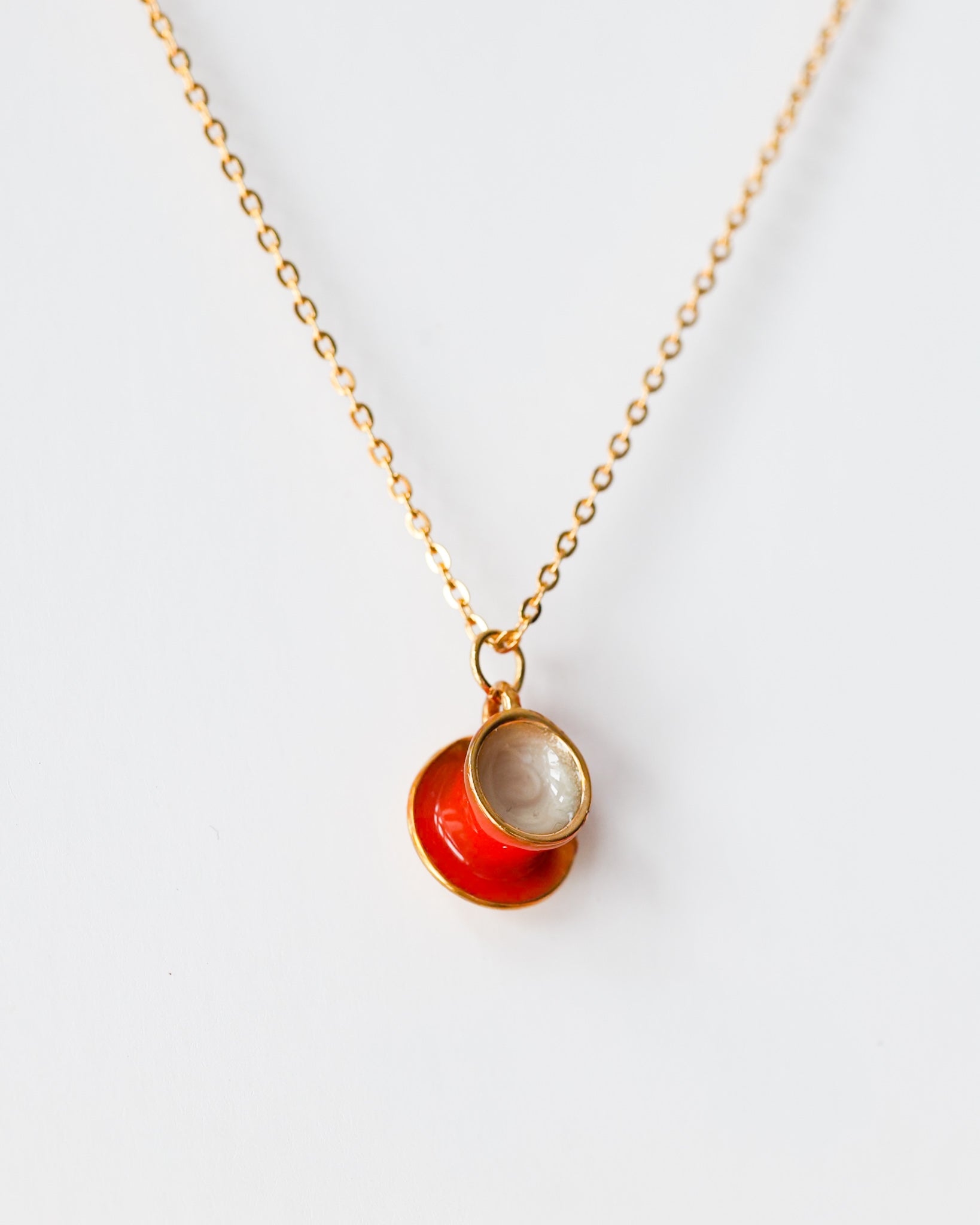 Gold chain necklace with a red enamel teacup and saucer pendant on white background