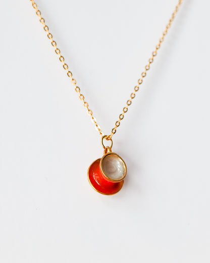 Gold chain necklace with a red enamel teacup and saucer pendant on white background