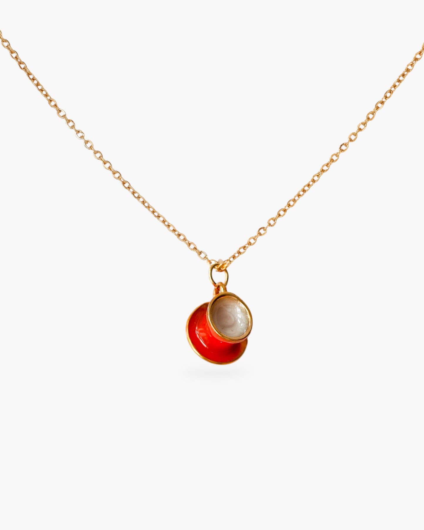 Gold minimalist necklace with red and pearl pendant on white background.
