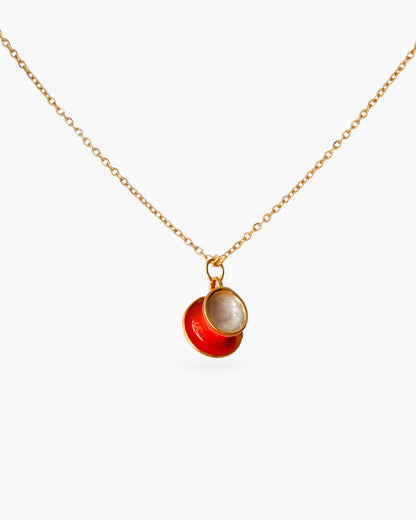 Gold minimalist necklace with red and pearl pendant on white background.