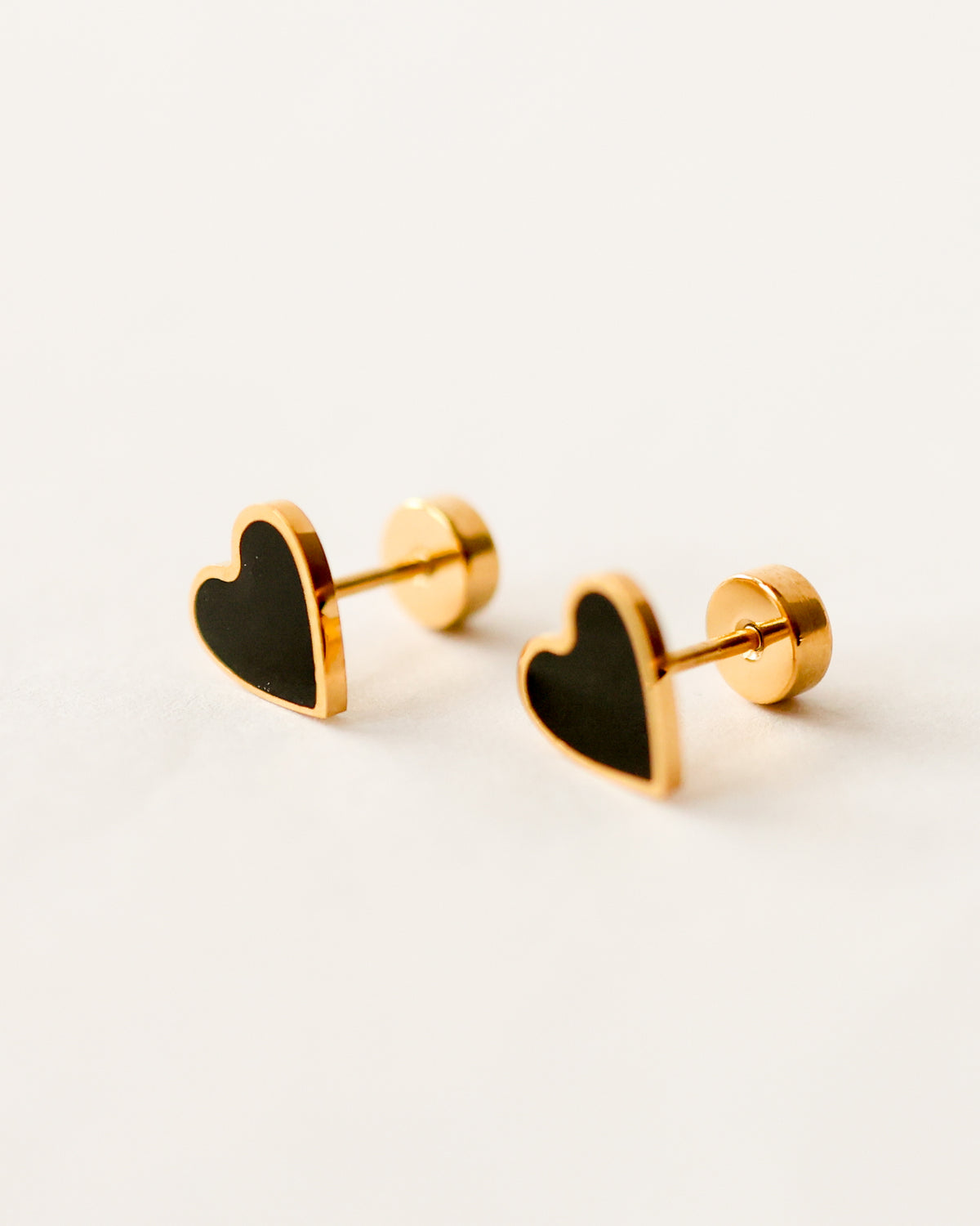 Minimalist gold heart stud earrings with black enamel on white background