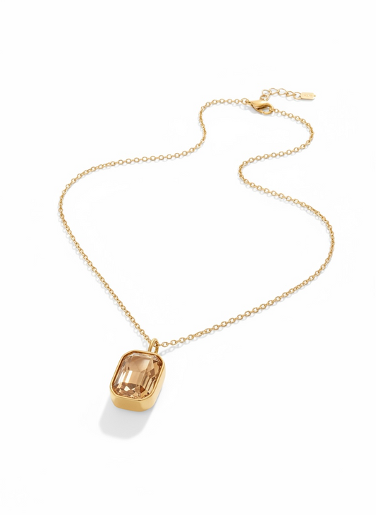 Gold chain necklace with a rectangular faceted gemstone pendant on white background