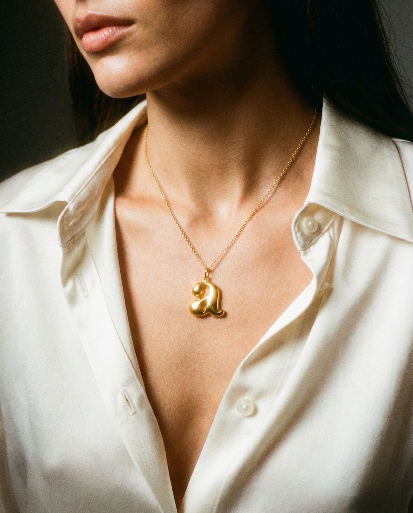 Gold letter pendant necklace on model wearing white silk shirt, minimalist jewelry
