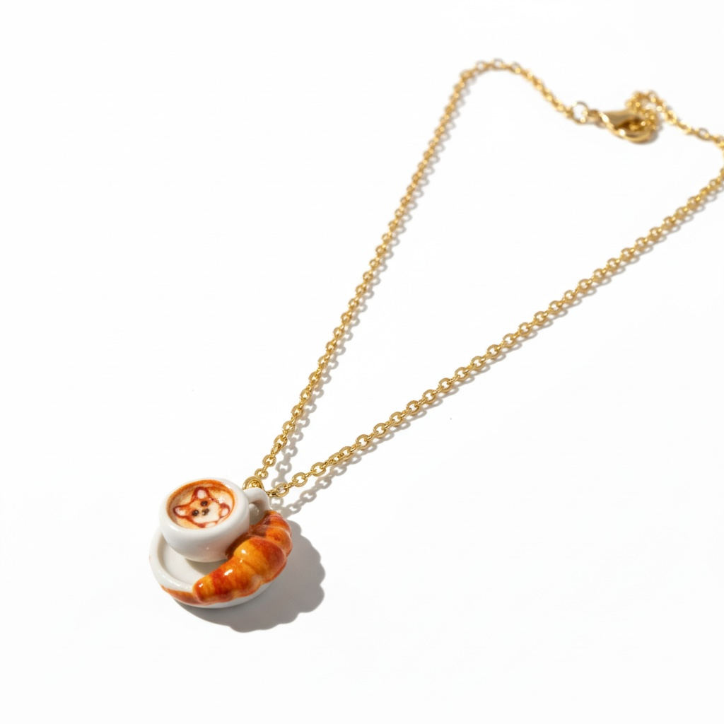 Gold chain necklace with a latte art and croissant charm on white background