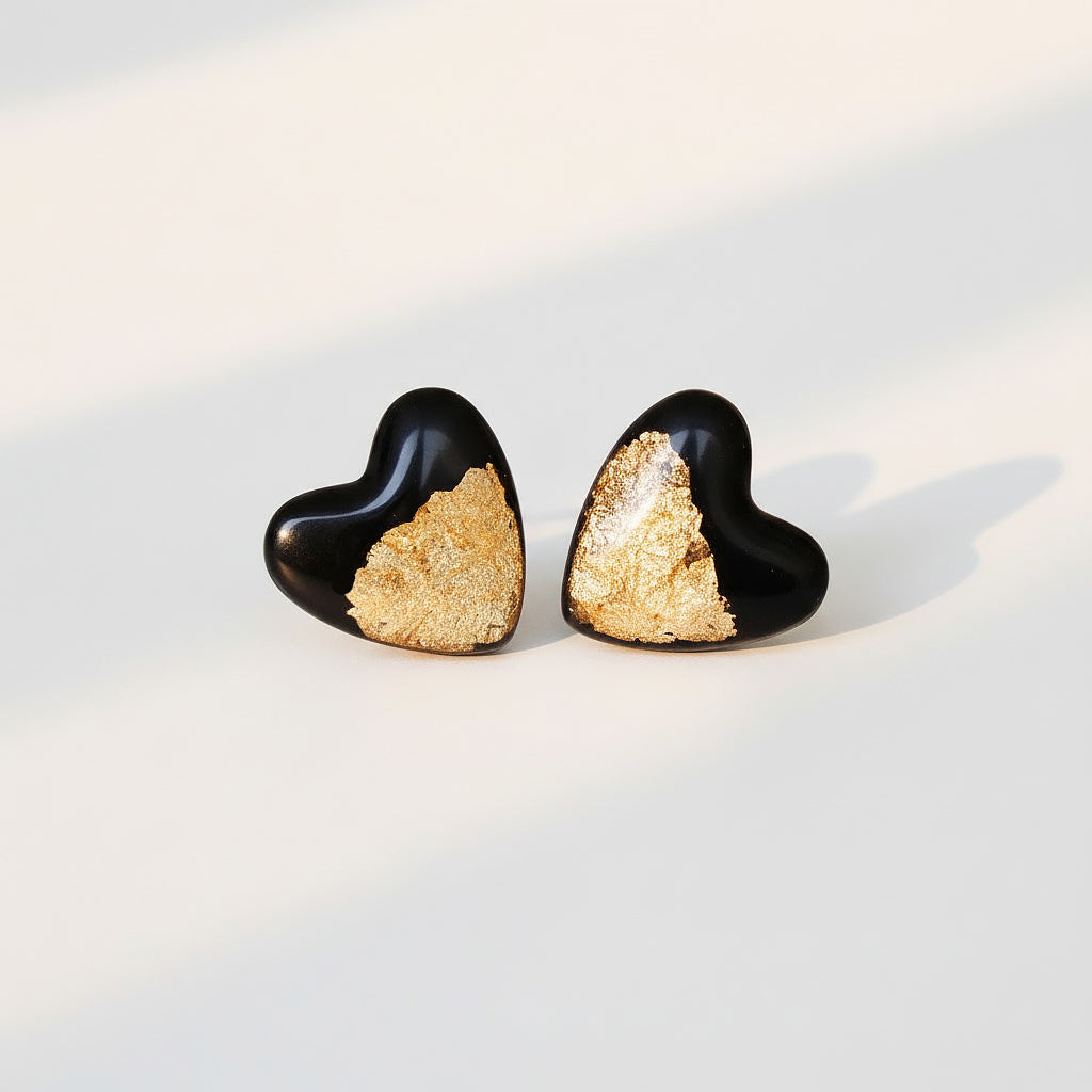 Black heart stud earrings with gold foil detail for sensitive ears on a light background