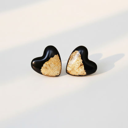 Black heart stud earrings with gold foil detail for sensitive ears on a light background