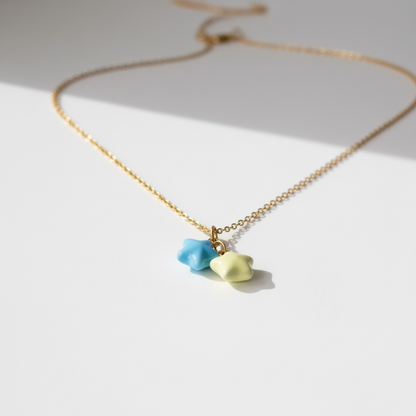 Gold necklace with blue and yellow star-shaped charms on a white background, minimalist jewelry
