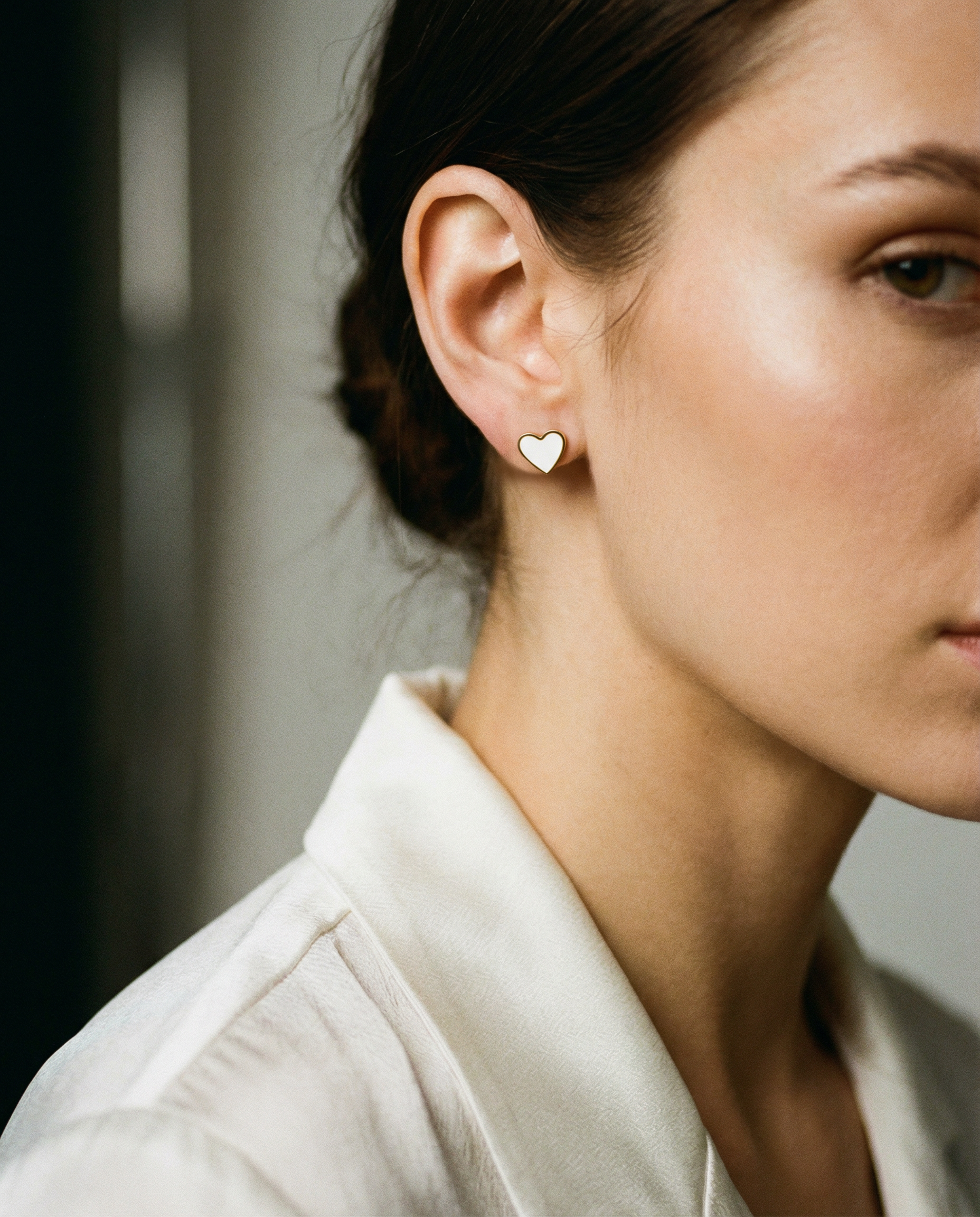 Minimalist flat back heart stud earrings worn by woman with neutral blouse