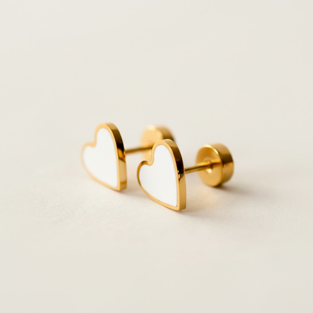 Gold heart stud earrings with white enamel on a light background, minimalist jewelry