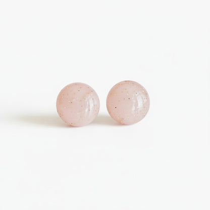 Minimalist pink round stud earrings with gold flecks on a white background