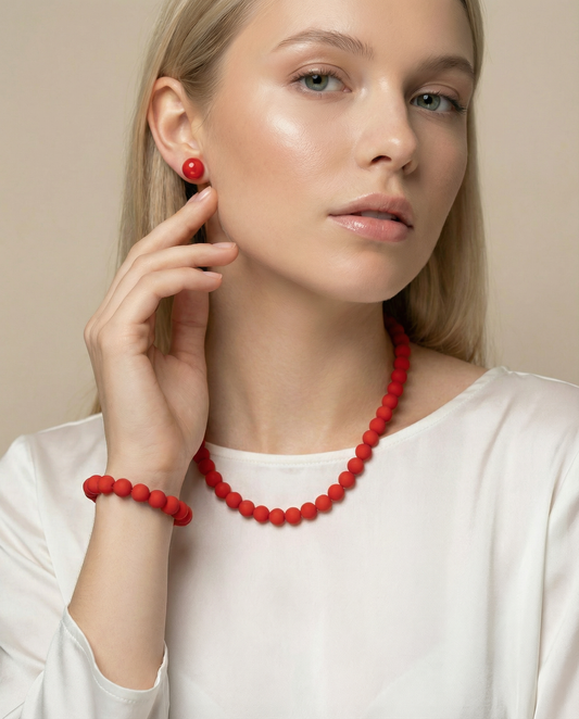 Woman wearing red bead necklace, red stud earrings, and matching bracelet, minimalist jewelry
