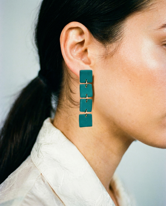 Teal earrings worn by a person with a neutral background