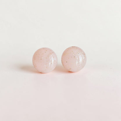 Round minimalist stud earrings with pale pink color and subtle glitter accents