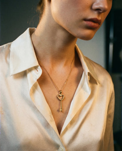 Close-up of a person wearing a gold necklace with a heart-shaped key pendant.