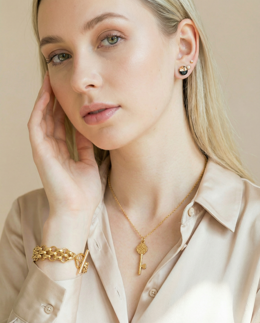 Woman wearing a chunky gold bracelet, key pendant necklace, and minimalist gold stud earrings