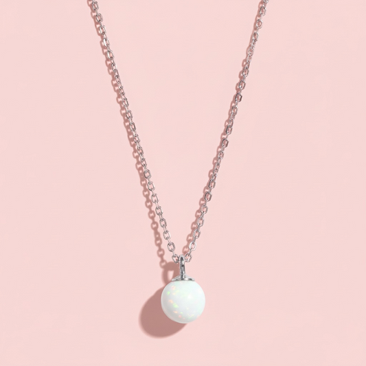 Minimalist silver chain necklace with a round white opal pendant on a pink background