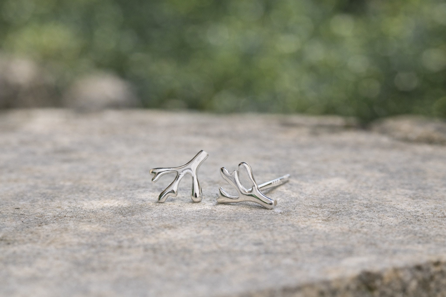 Handmade minimalist silver branch stud earrings displayed on natural stone