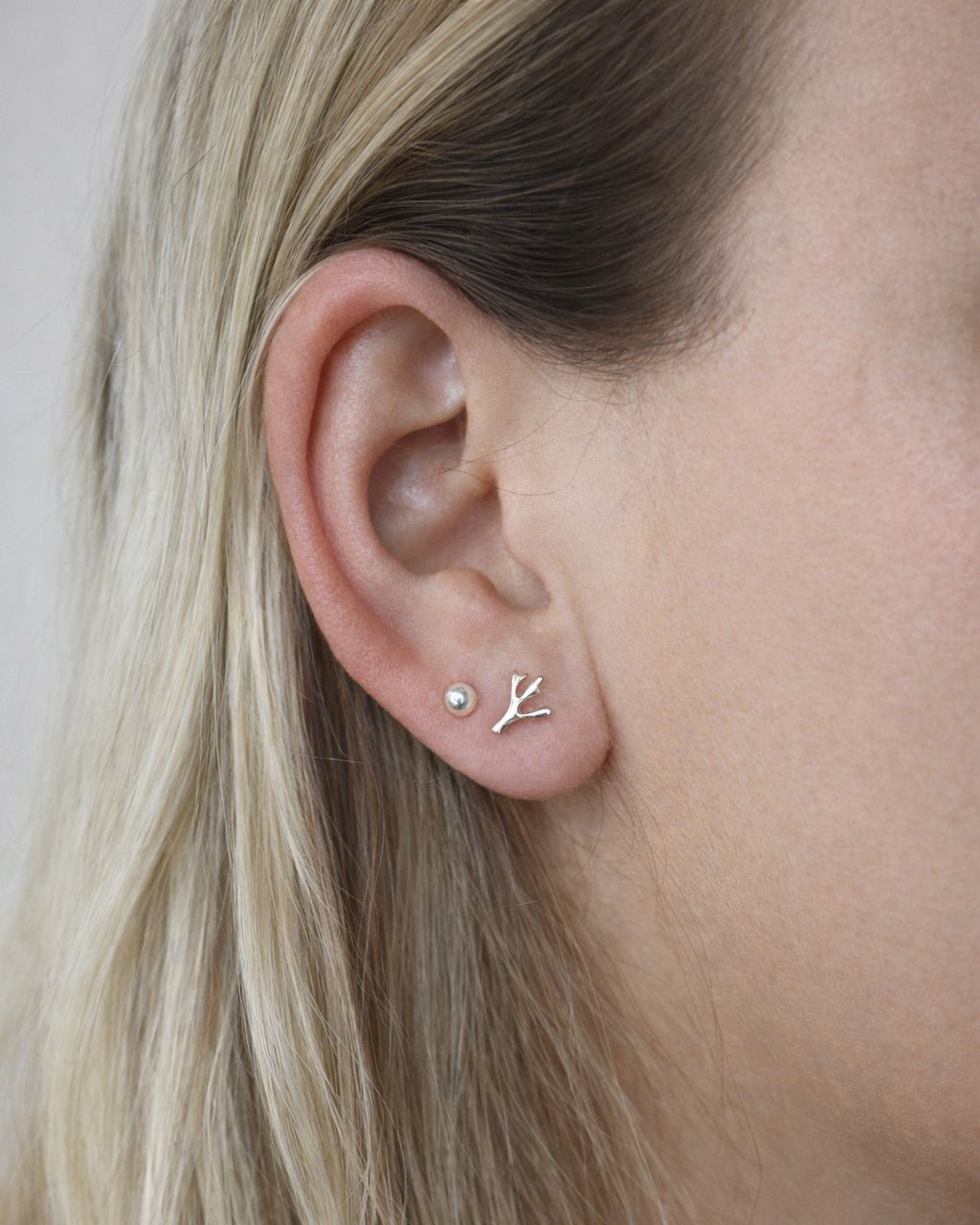Minimalist silver stud earrings on ear, one round and one branch-shaped, handmade jewelry