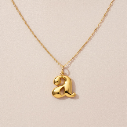 Gold necklace with lowercase letter a pendant on light background, minimalist jewelry