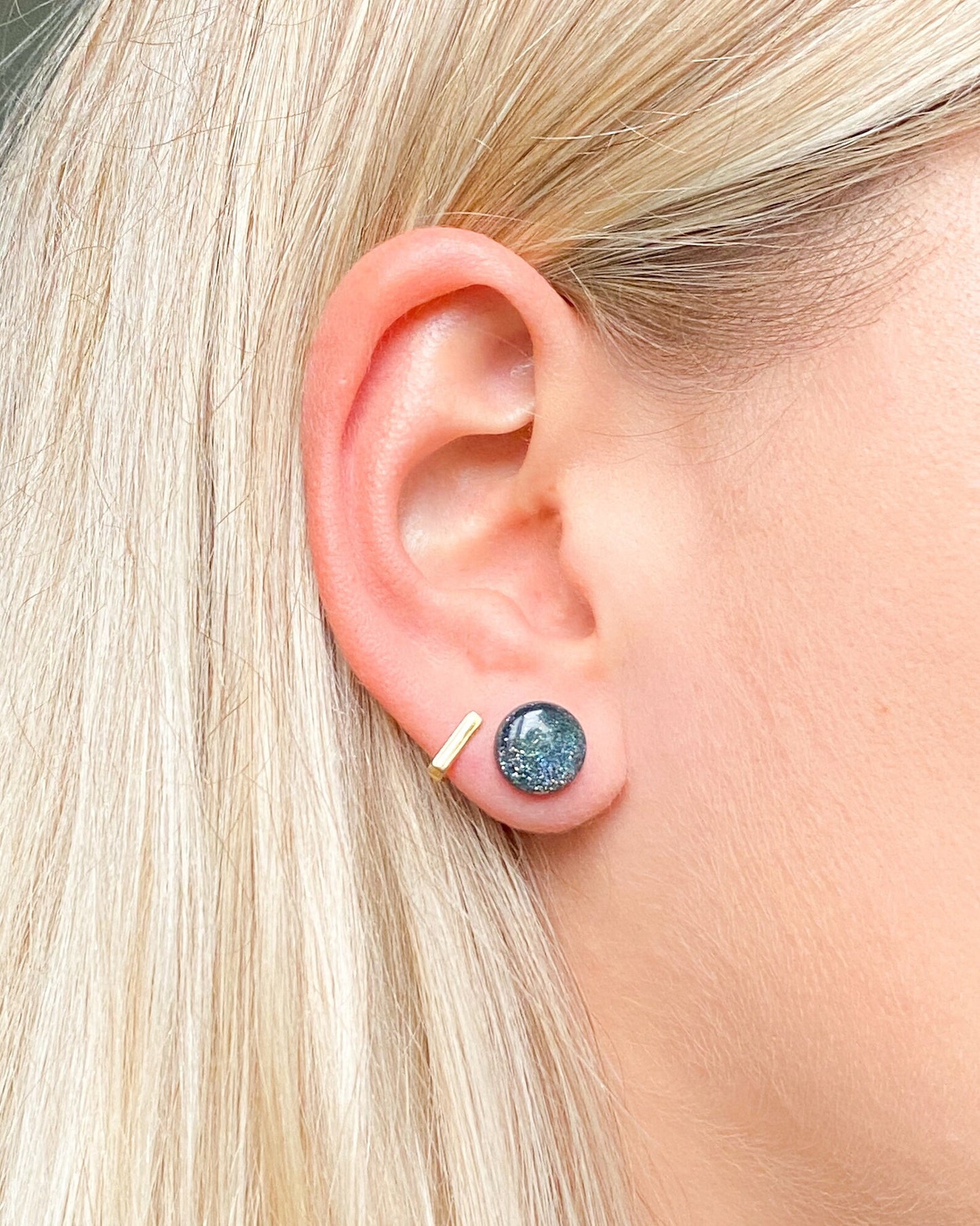 Close-up of an ear wearing a blue gemstone stud earring with a gold post.