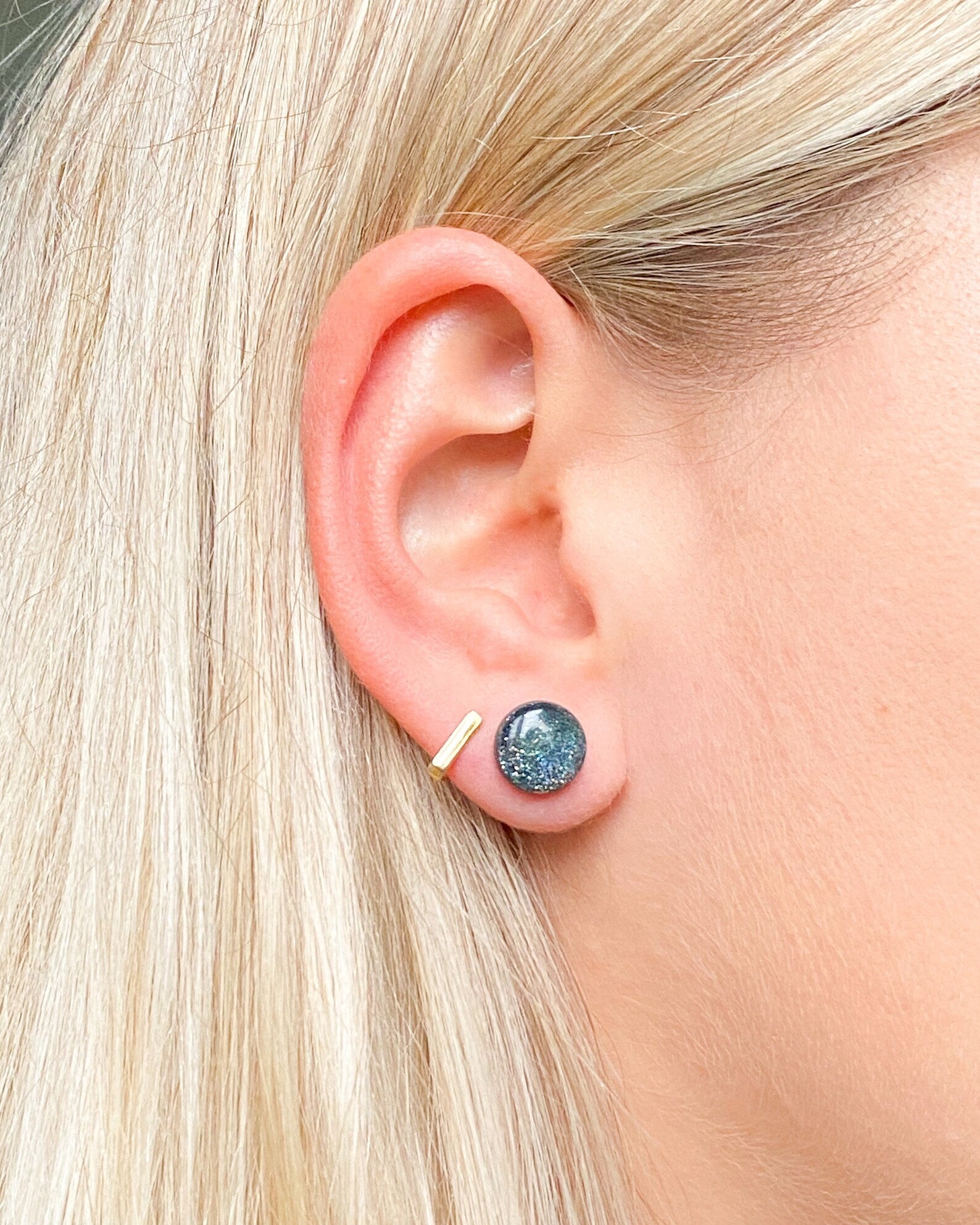 Close-up of an ear wearing a blue gemstone stud earring with a gold post.