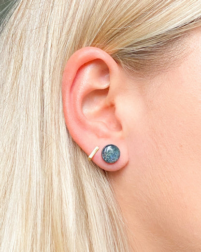 Close-up of an ear wearing a blue gemstone stud earring with a gold post.