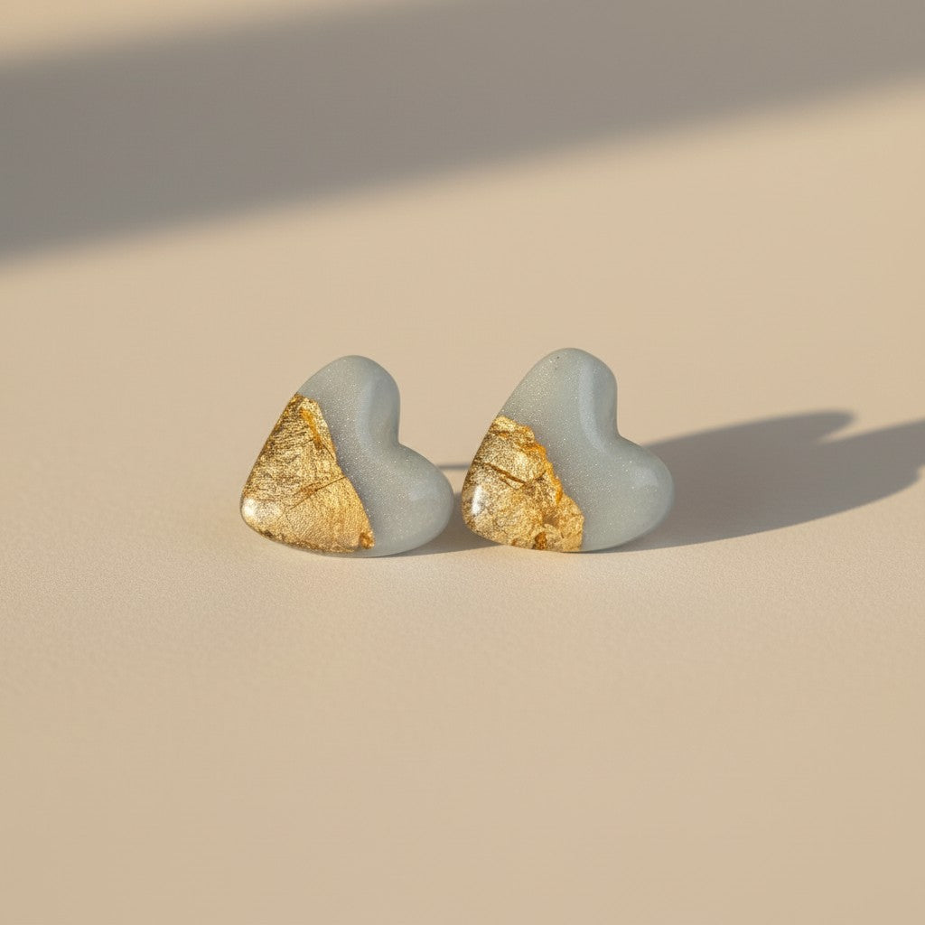 Sky blue heart stud earrings with gold leaf accent on neutral background