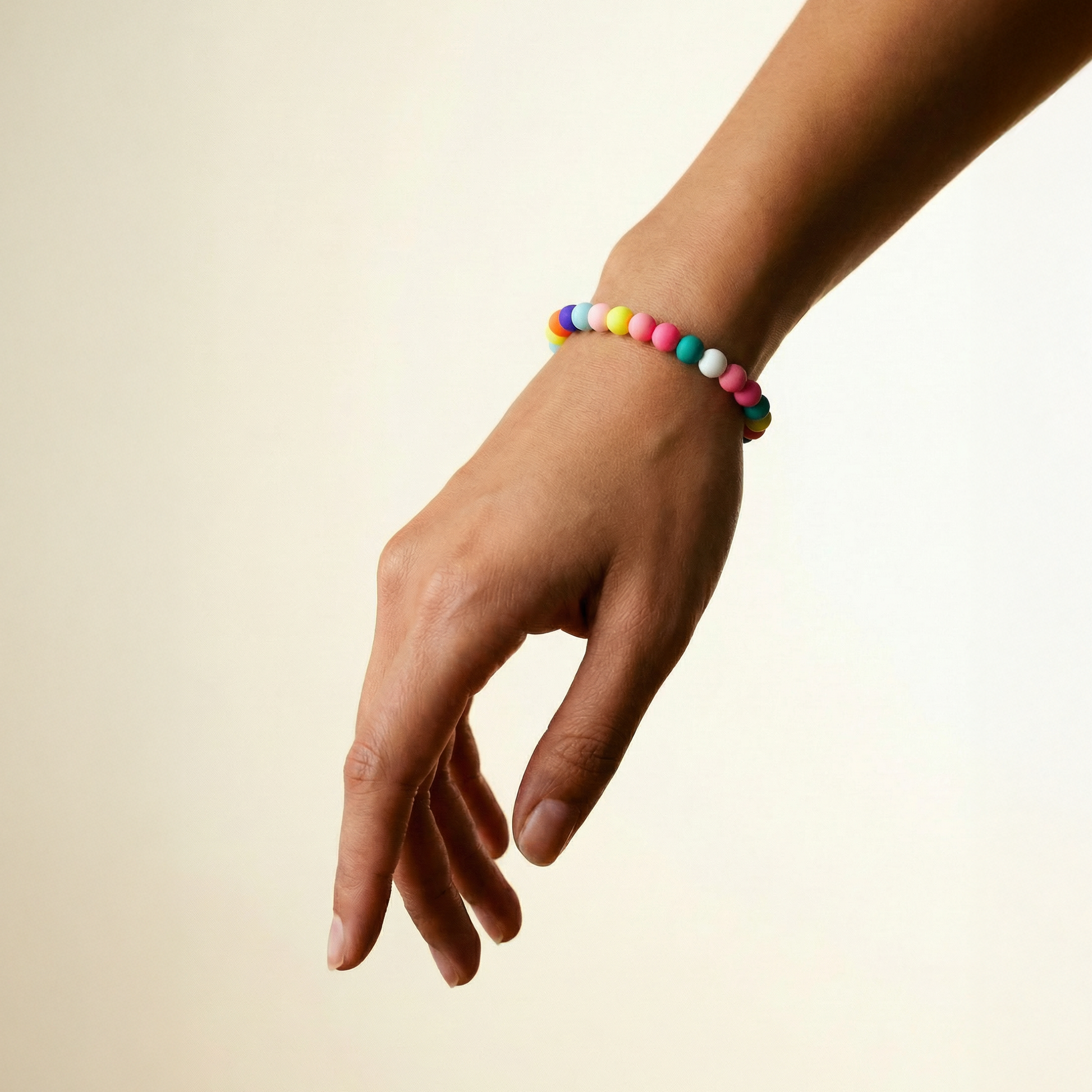 Hand wearing a colorful beaded bracelet on a beige background