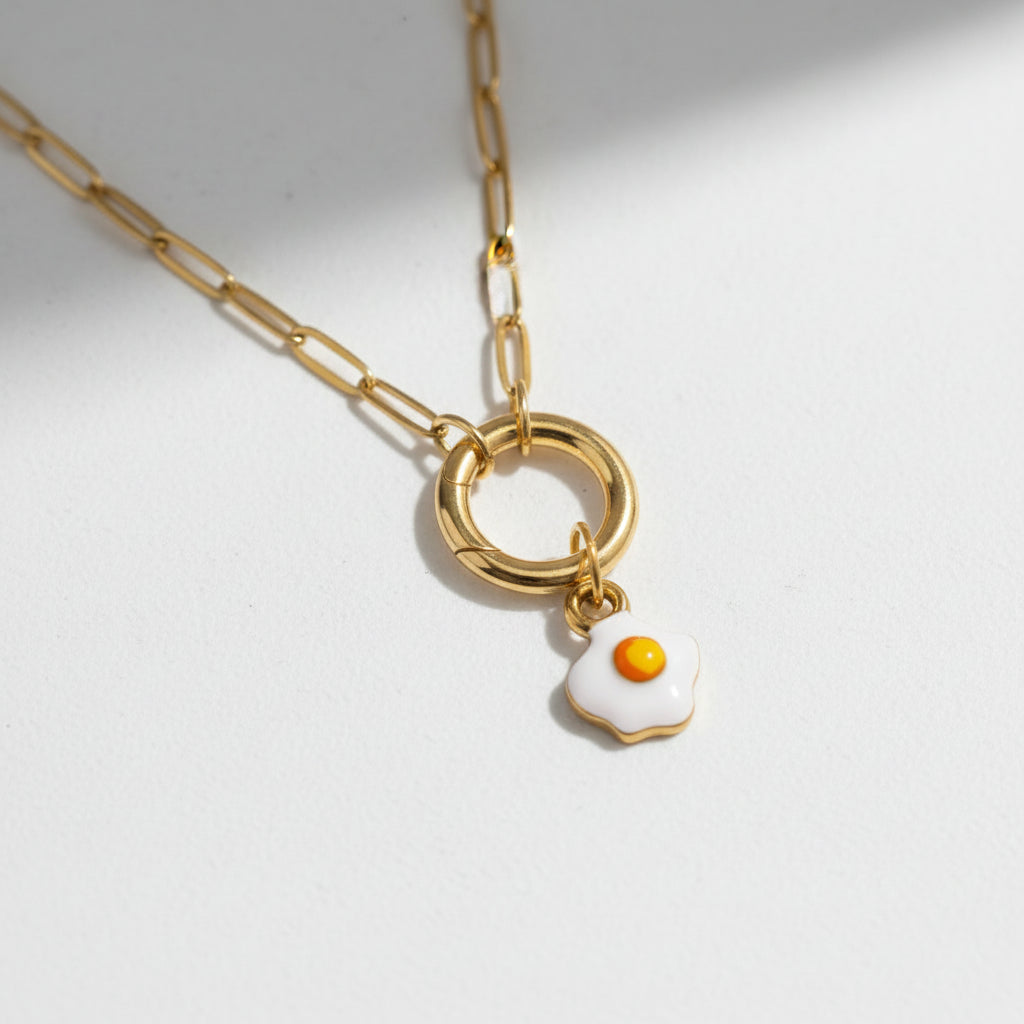 Gold chain necklace with small fried egg pendant on white background