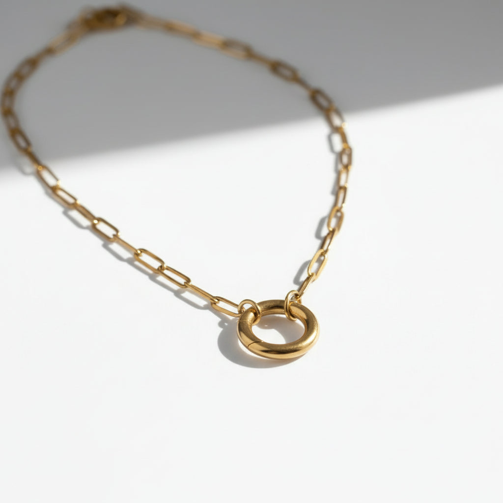 Minimalist gold chain necklace with round pendant on white background.