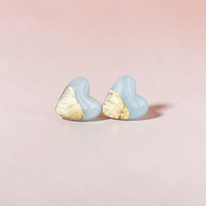 Handmade light blue heart stud earrings with gold accent on a pink background