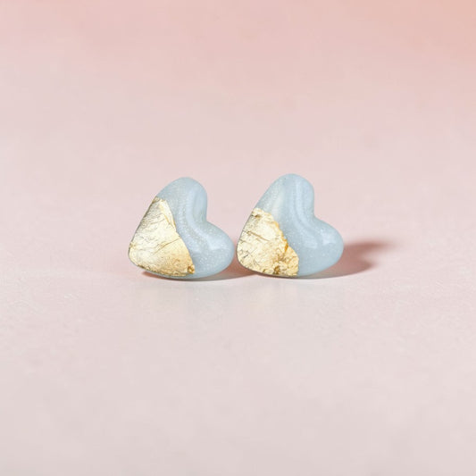 Handmade light blue heart stud earrings with gold accent on a pink background