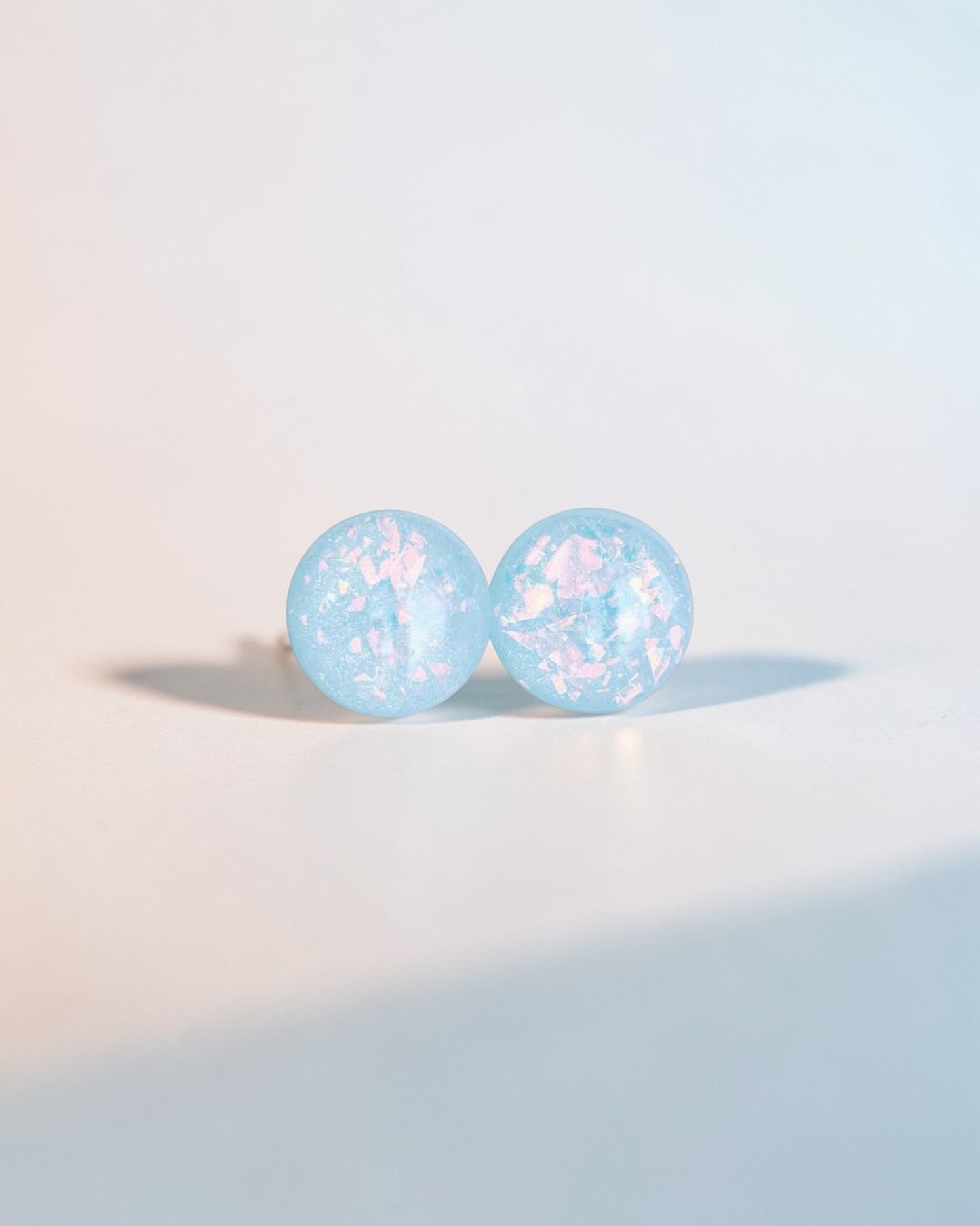 Handmade minimalist blue stud earrings with iridescent flakes on a light background