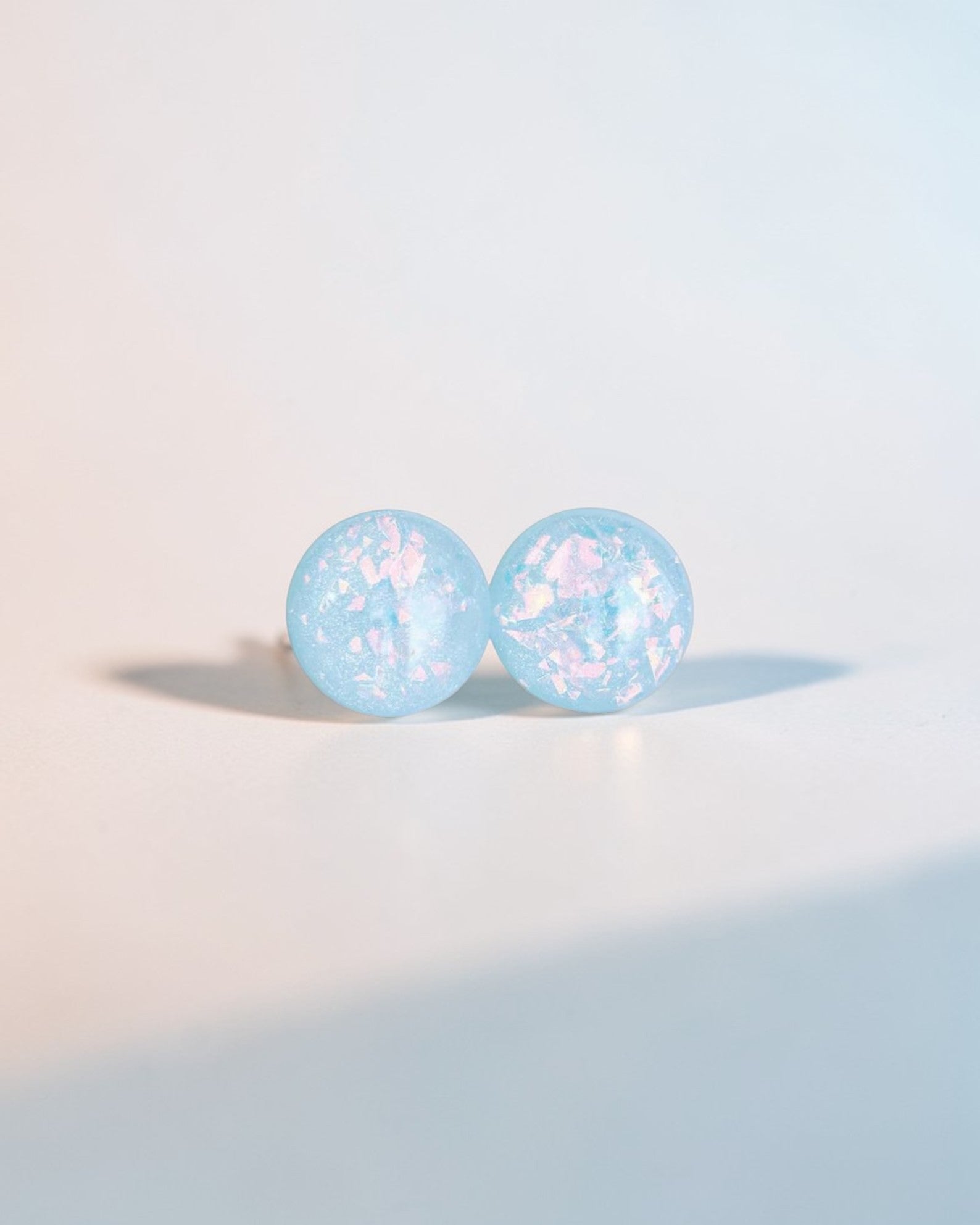 Handmade minimalist blue stud earrings with iridescent flakes on a light background