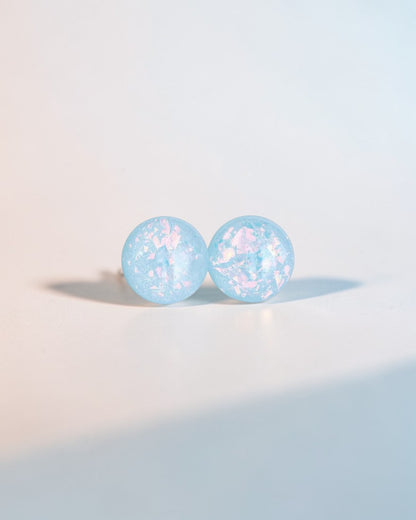 Handmade minimalist blue stud earrings with iridescent flakes on a light background