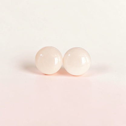 Minimalist pale pink round stud earrings on a soft neutral background